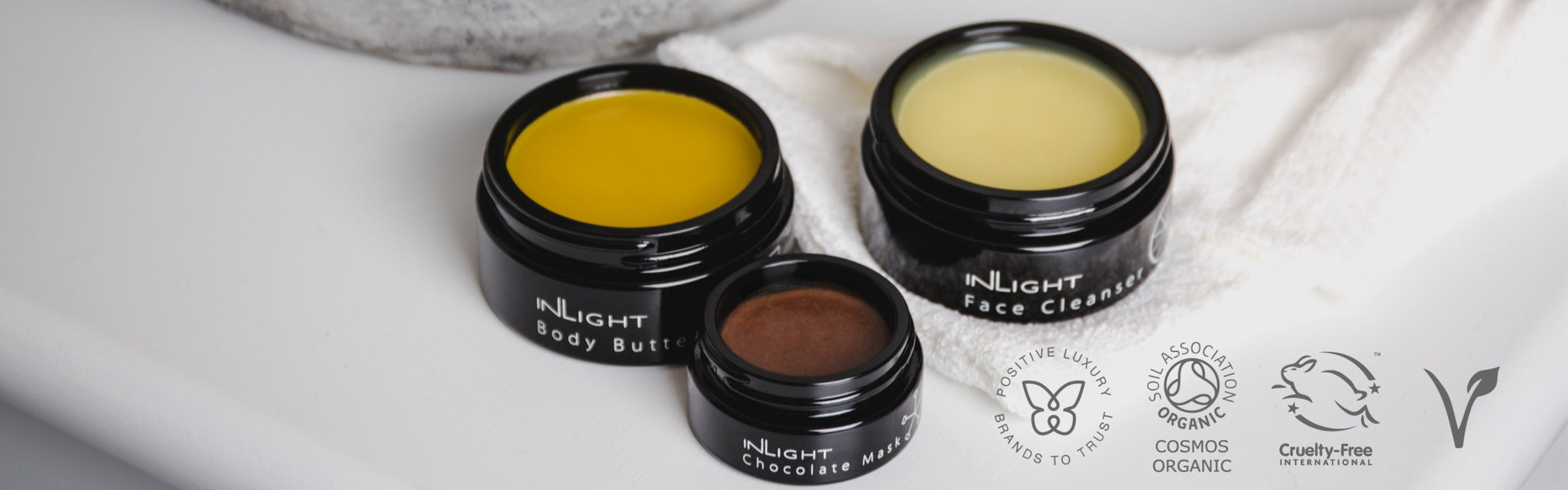 Inlight Beauty - Waterless Skincare & Beauty Collection. Image shows a woman holding two Inlight boxes and with a spot of Inlight waterless facemask on each of her cheeks. 