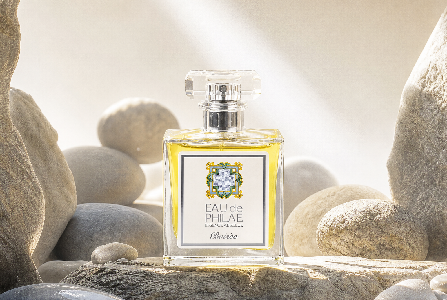A rectangular glass perfume bottle with a clear cap stands centered among smooth river stones and large rocks. The bottle contains a pale golden liquid. Organic men's cologne sold by Inlight Beauty