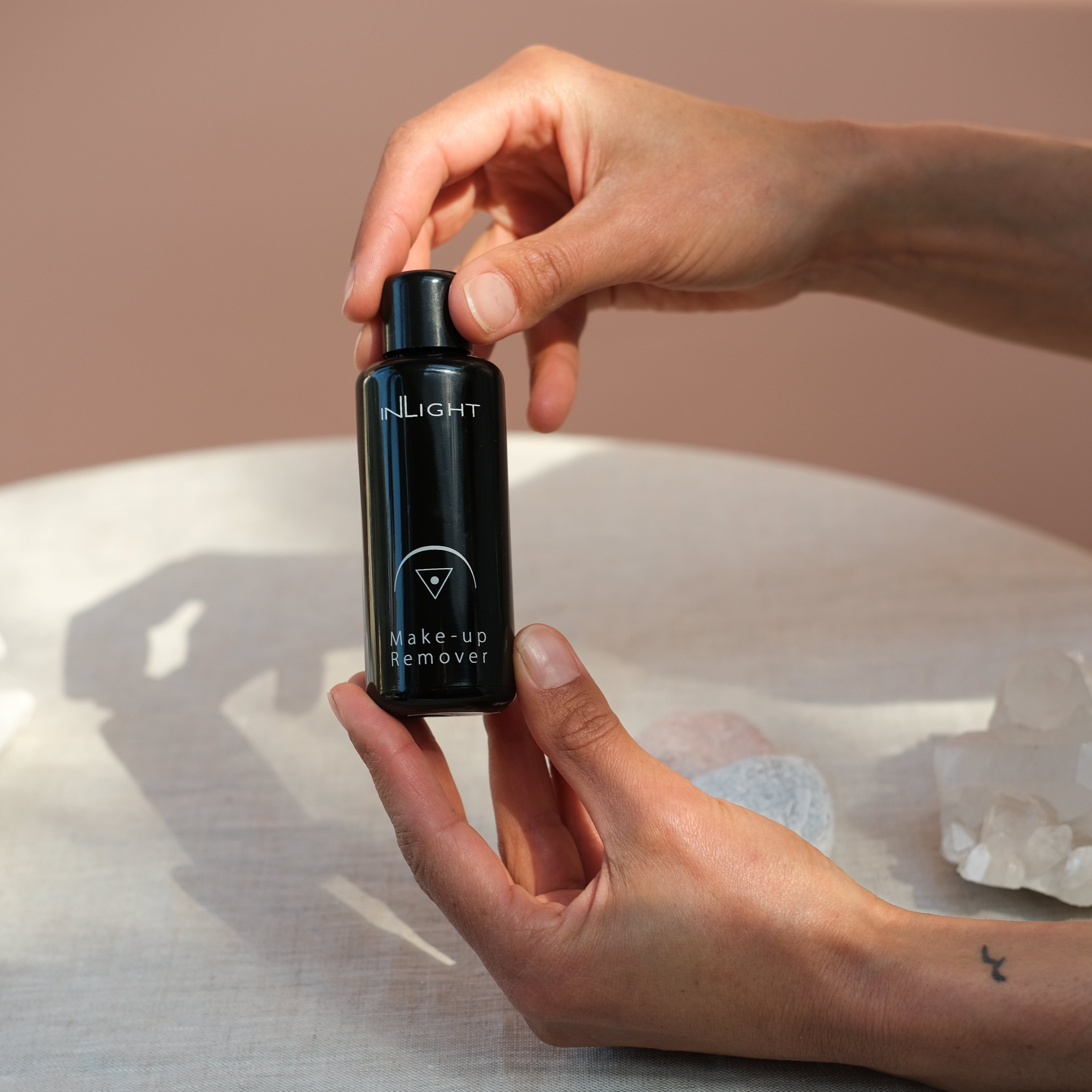 Model holding black miron bottle of organic Make-up Remover. Inlight Beauty