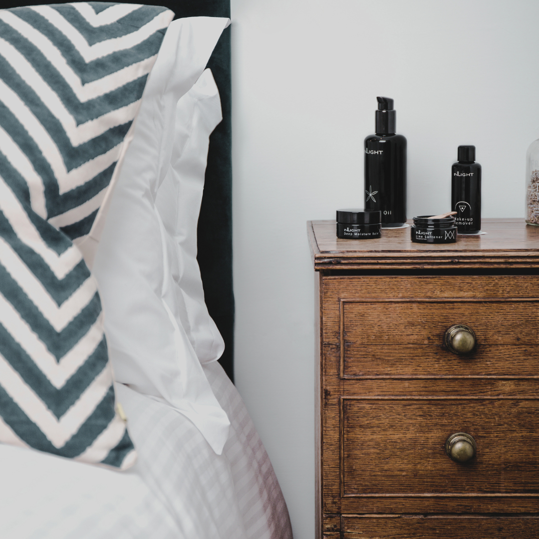 Wooden dresser with Inlight Beauty organic skincare products next to a bed with striped pillows