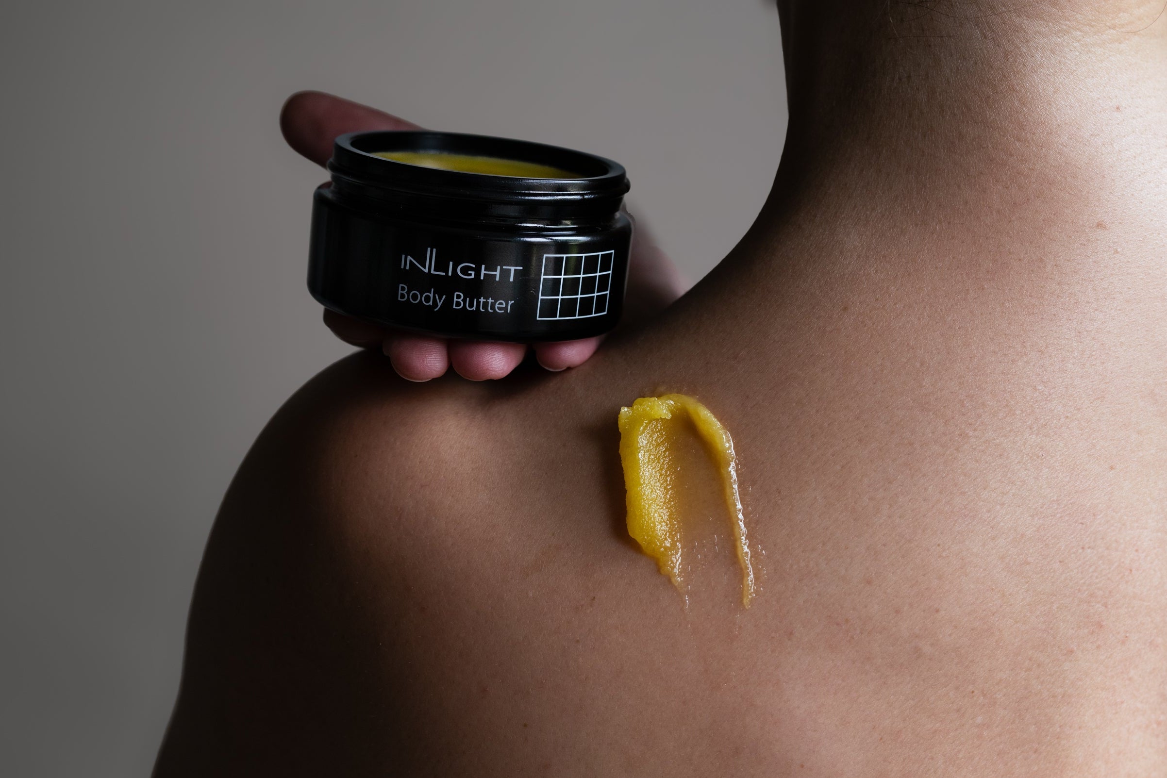Person applying INLIGHT Body Butter to their shoulder with a visible smear on skin.